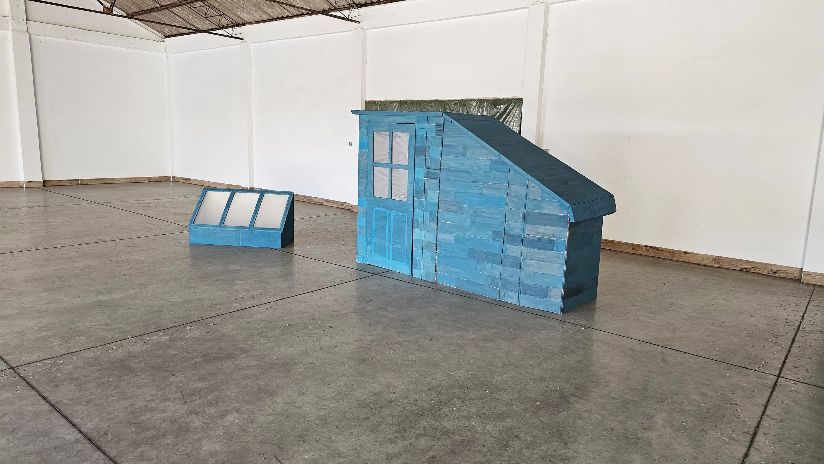 La caseta de azotea terminada, pintada de azul a mano, junto a su claraboya, exenta en mitad de la nave.